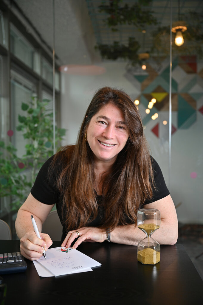 צילומי אווירה בבית העסק, יועצת משכנתה כותבת ליד שולחן משרדי עם שעון חול שמייצר עניין ויזואלי